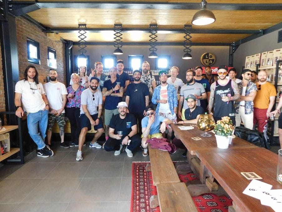 a group of tourists smiling happily at the camera at Pineios Brewery tasting room and in front of them a wood table